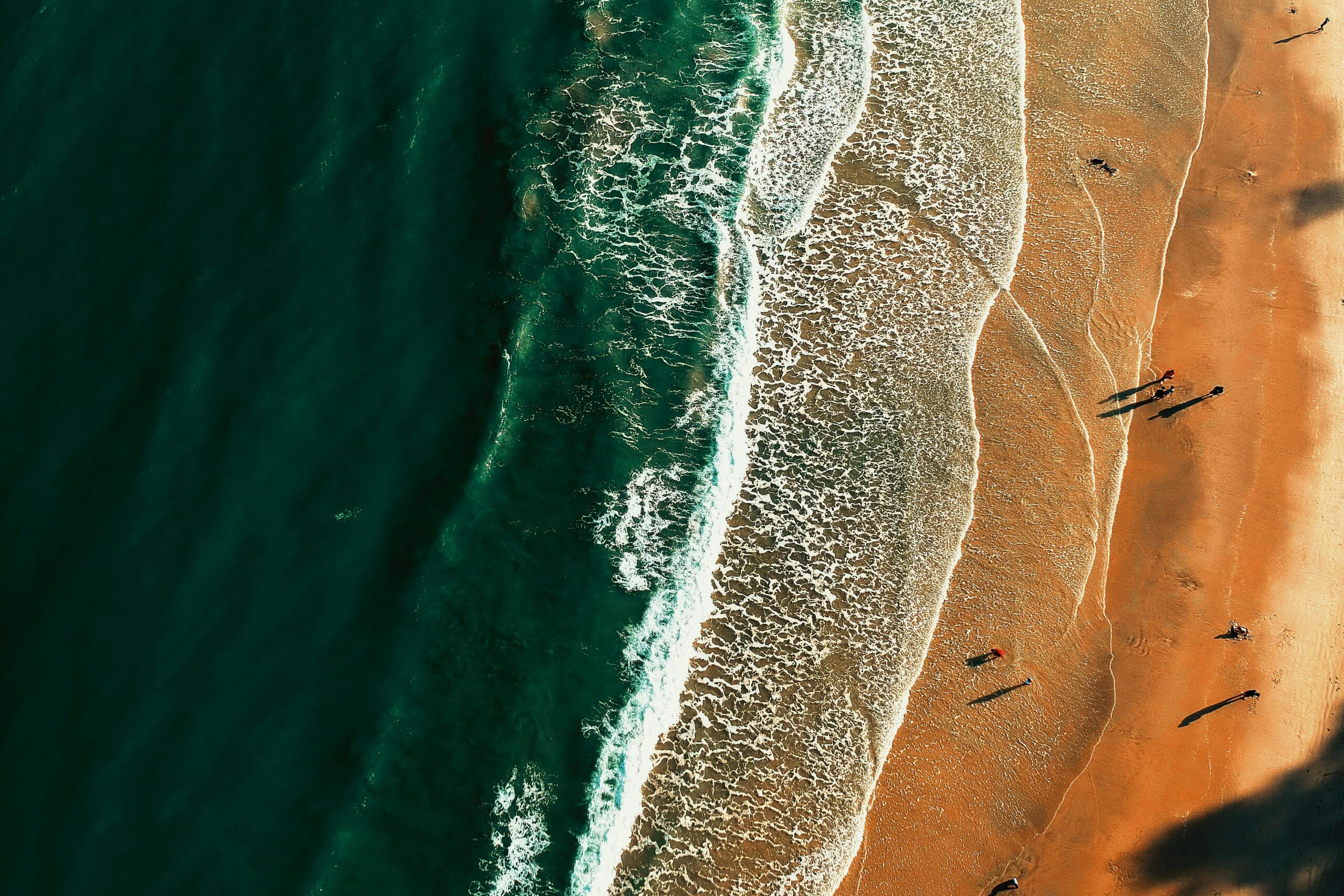 A stunning aerial perspective of a beach with crashing waves and shadows cast on the golden sand.