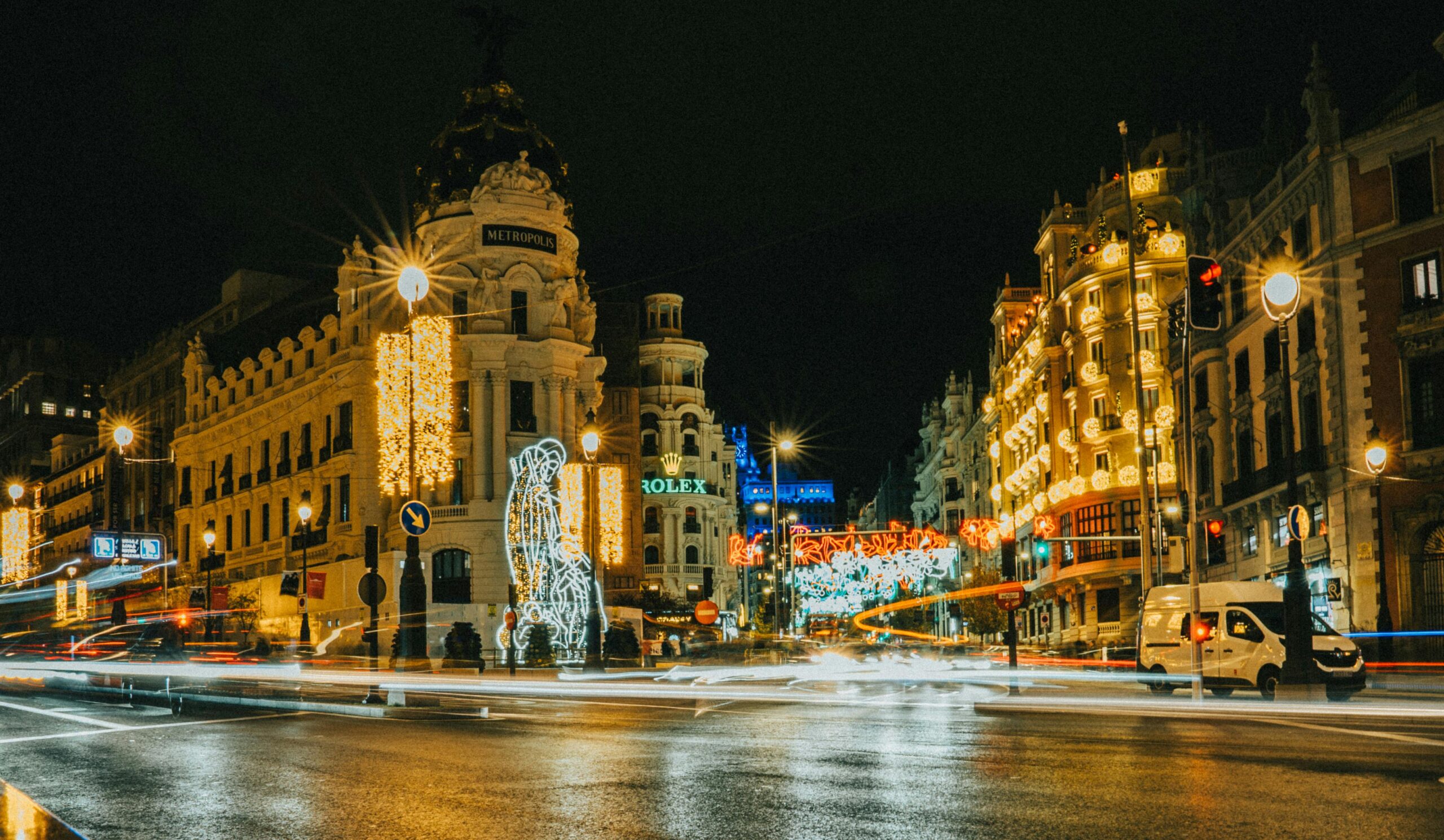 Stunning nighttime view of Gran Via in Madrid with festive holiday lights illuminating the iconic Metropolis building.