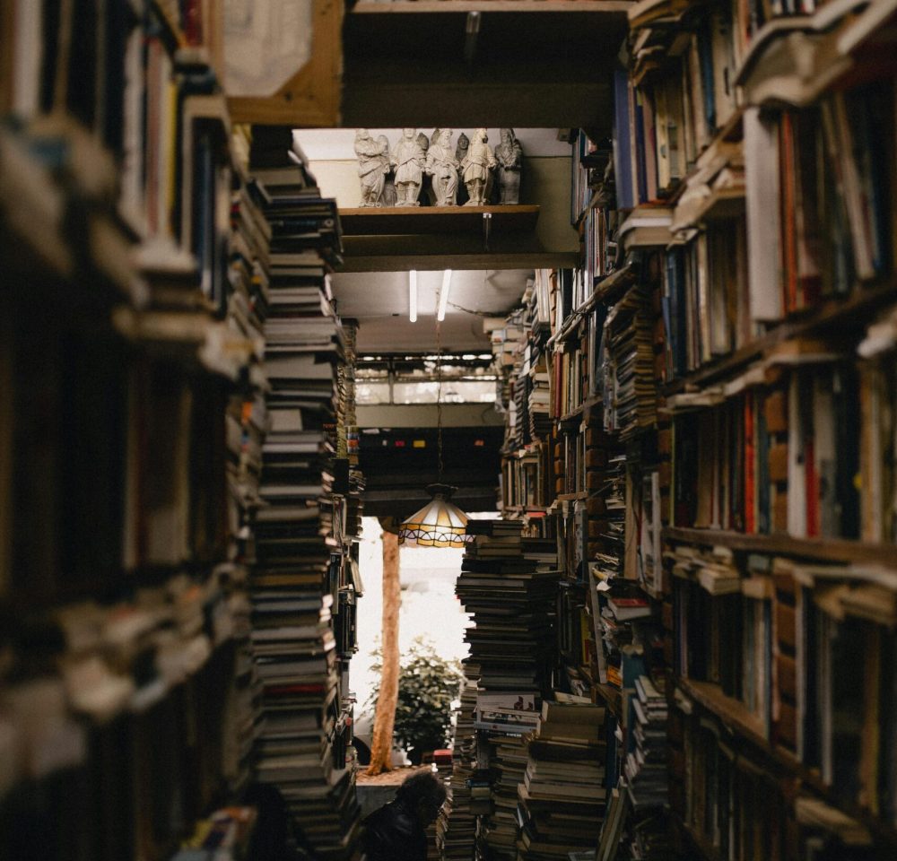 A densely packed library aisle with numerous stacks of books creating a warm and inviting atmosphere.