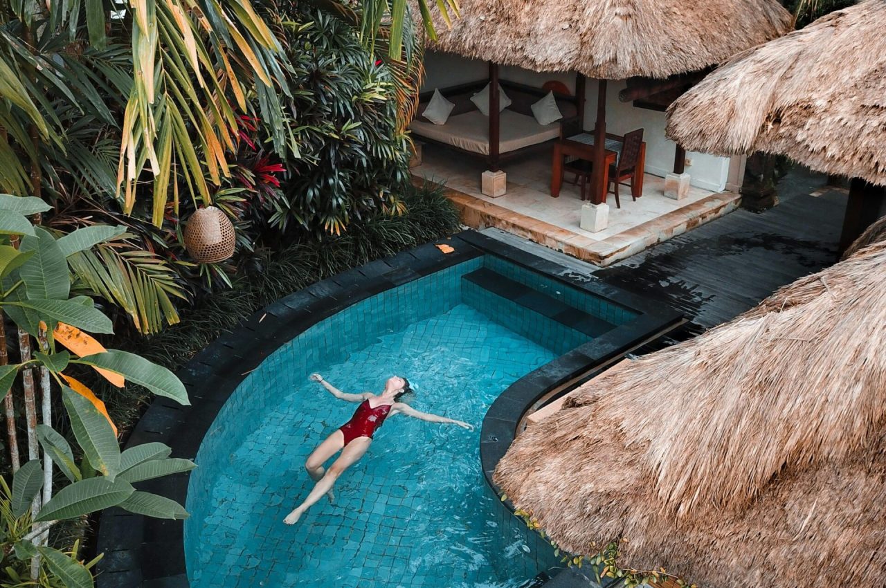 A woman enjoying leisure time floating in a tropical resort pool surrounded by lush greenery.